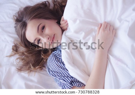 Beautiful young woman waking up fully rested. Rest, sleeping, comfort and people concept - teen girl lying in the bed at home bedroom in the morning and smiling after wake up. View from above.