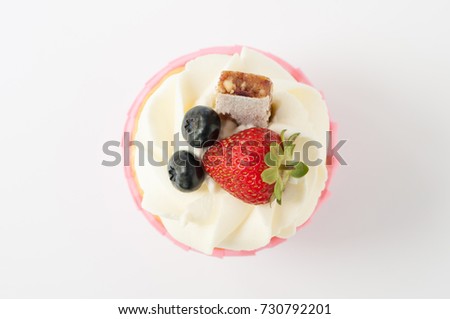 Pink cupcake with white whipped cream decorated with strawberry, blueberry, granola bar on white background. Picture for a menu or a confectionery catalog. Top view.