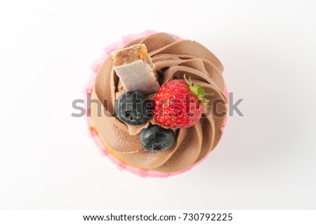 Pink cupcake with chocolate whipped cream decorated with strawberry, blueberry, granola bar on white background. Picture for a menu or a confectionery catalog. Top view.