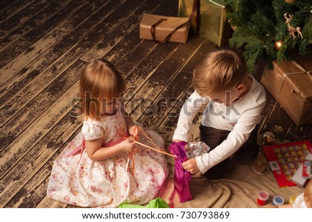 Adorable Caucasian children sitting next to Christmas tree. Two kids having fun together, opening gift boxes.  