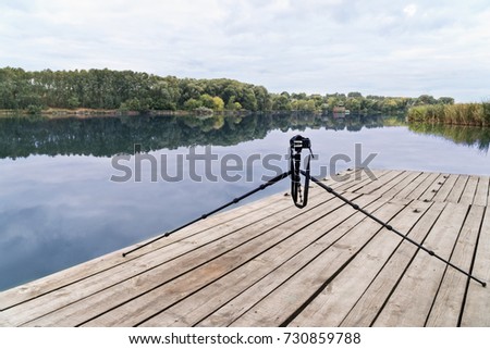 Digital camera standing on a tripod on a wooden platform near the lake