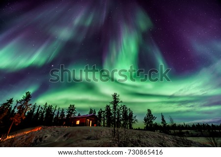 Amazing Aurora in purple and blue color dancing over chalet in Yellowknife Royalty-Free Stock Photo #730865416