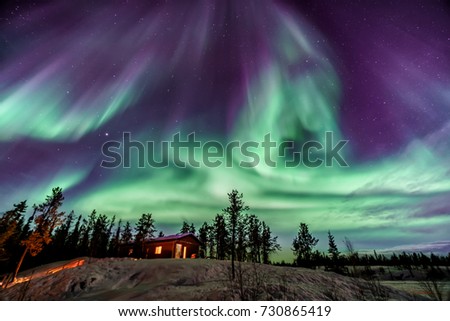 Amazing Aurora in purple and blue color dancing over chalet in Yellowknife Royalty-Free Stock Photo #730865419