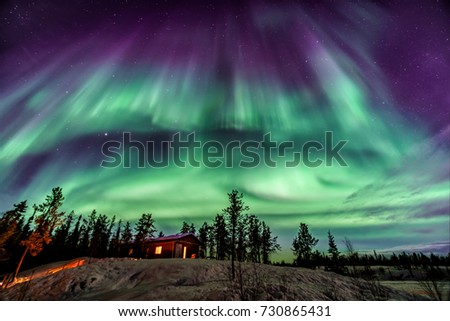 Amazing Aurora in purple and blue color dancing over chalet in Yellowknife Royalty-Free Stock Photo #730865431