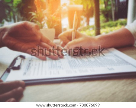 The blurry light design background of human hand with pen is signing on The Insurance Claim Form,on wooden desk,vintage tone.