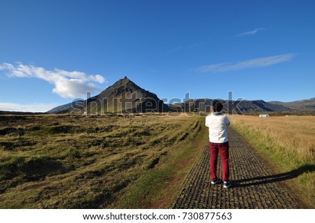 Back view of Asian man using his cell phone taking picture of beautiful view of Bardur Snaefllsas, the mythical protector of the Snaefellsnes Peninsula with Mt Stapfell as background.