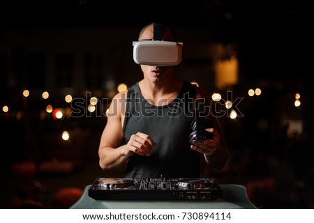 Handsome muscular nightclub DJ in night vision glasses with headphones plays the music on the background of lights