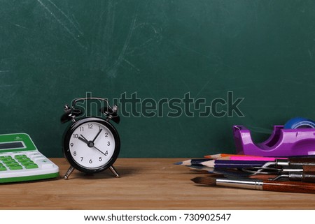 Office supplies and clock on desk, chalkboard background