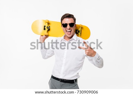 Portrait of a cheerful amused man in white shirt and sunglasses posing with a skateboard and showing peace gesture while standing and looking at camera isolated over white background