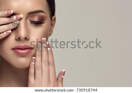 Beautiful model girl with a beige French manicure nail design with rhinestones . Fashion makeup and care for hands and nails and cosmetics . Royalty-Free Stock Photo #730918744