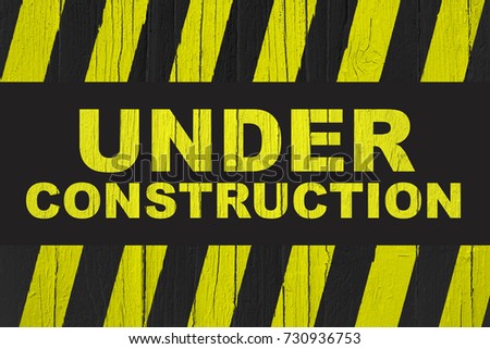 Under construction warning sign with yellow and black stripes painted over cracked wood. Sign usually used in construction sites meaning: do not enter the area, caution, danger