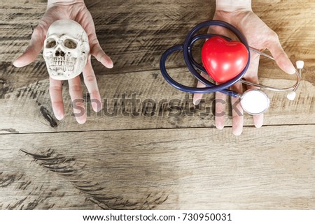 Stethoscope and red heart on left hand, skull on right hand. Choosing healthcare and die concept with free copy space for text.