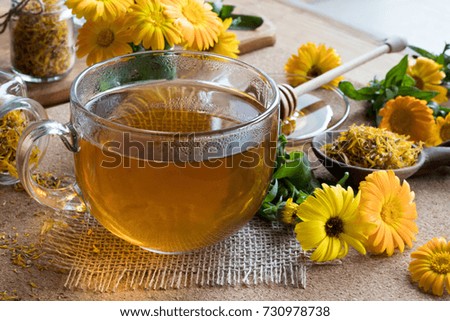 A cup of calendula (marigold) tea on a wooden table, with fresh and dry calendula flowers in the background