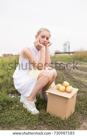 slender blonde girl sells apples in autumn Park. troubled skin and pimples, hair in a bun. emotional portrait. a sad and depressive mood. Wallpapers for your desktop. street style in clothes