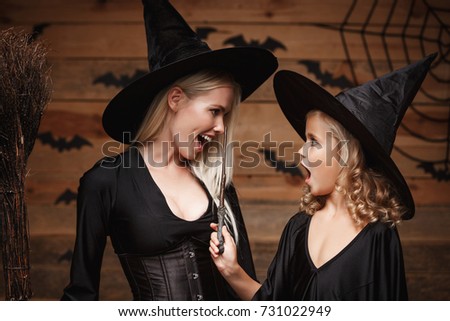 Halloween Concept - Closeup beautiful caucasian mother and her daughter in witch costumes celebrating Halloween posing with curved pumpkins over bats and spider web on Wooden studio background.