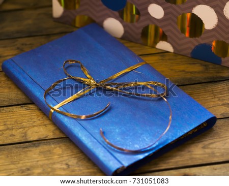 The book lies on a wooden background, in a gift, blue wrapper with a gold bow