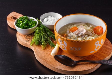 Homemade chicken noodle soup in a bowl on a wooden cutting board with salt shaker, chopped green onions and dill Royalty-Free Stock Photo #731052454
