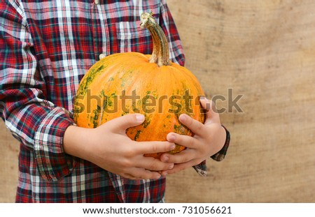 The child is holding an large orange pumpkin
