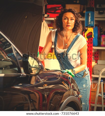 beautiful woman in the garage near the car with an open hood. woman auto mechanic in blue overalls. instagram image filter retro style