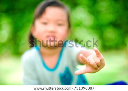 A little cute asian girl show hand in shape of love (i love you) and smile on the green grass background. (Selective focus-a hand)