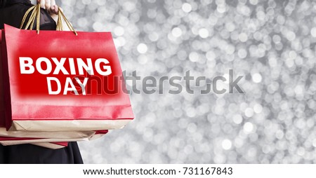 Young woman holding boxing day shopping bag on silver bokeh background Royalty-Free Stock Photo #731167843