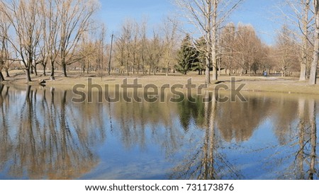 Beautiful spring landscape. Blue lake with reflection of trees without foliage.