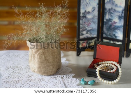 Still life mat vase with dry grass and jewelry box with pearl necklace on lace tablecloth