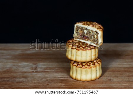 a pyramid of three Chinese lunar gingerbread cookies standing on a wooden board, behind a black background