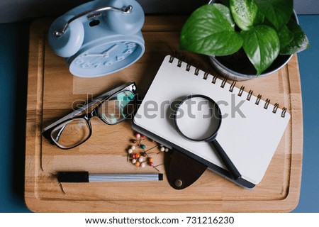 Alarm clock,green plant,spectacle pen and a note book on the wooden board view from top with space for your text.Business and financial concept.