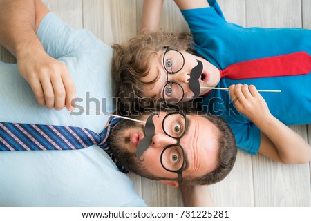 Funny man and kid with fake mustache. Happy family playing in home. Movember concept