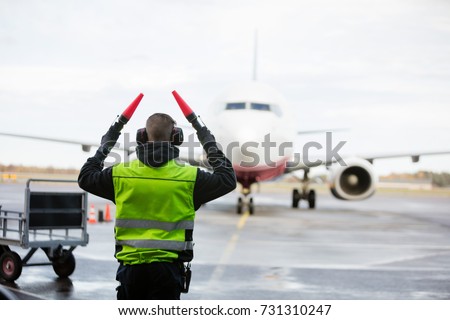 Ground Crew Signaling To Airplane On Wet Runway Royalty-Free Stock Photo #731310247