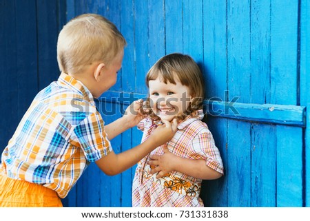 Brother tickling her sister. Little kids playing against blue wooden wall