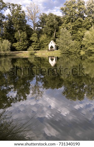 Beautiful photo of a white hut in the middle of the forest on a cloudy day reflected perfectly in a lake