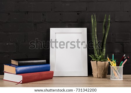 close up view of photo frame, office supplies, plant in flowerpot and books on wooden tabletop