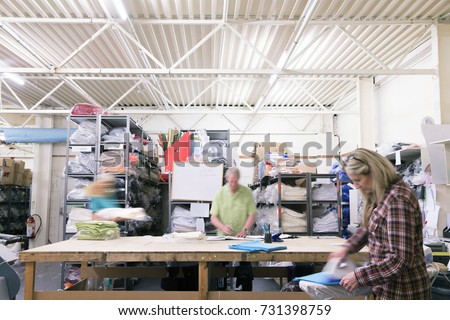 Busy workers in a textile factory. They are pressing and sorting fabric and material. 
