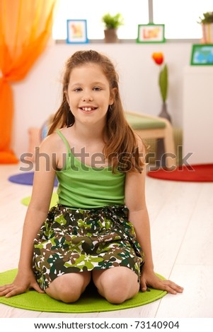 Portrait of smiling little girl sitting on floor at home, looking at camera.?
