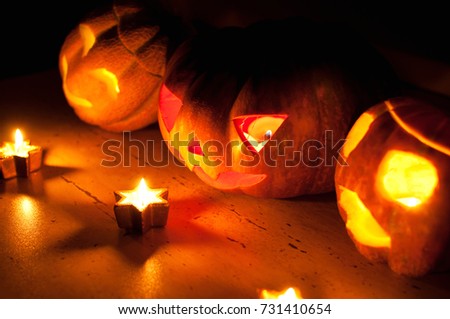 Scary halloween pumpkin and melon jack-o-lanterns on black background lit with small round and star candles. Selective focus, bokeh.