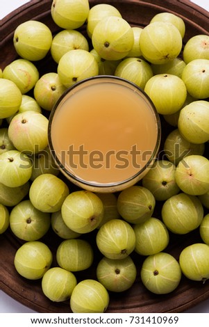 Fresh Gooseberry or Amla Juice (Phyllanthus emblica). Poured In a glass with whole Avla over colourful or wooden background. selective focus