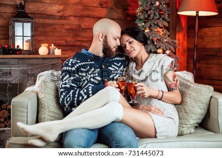 Beautiful couple sitting on the couch and holding a glass of mulled wine in a decorated festive interior with a Christmas tree. Concept of a family celebration, new year's eve