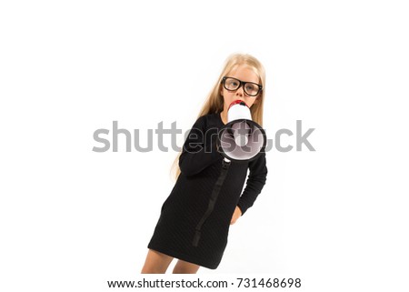 Isolated on white, pretty caucasian blonde little girl in black dress, glasses, black socks and white shoes stands and holds a megaphone, talk in it, look at camera
