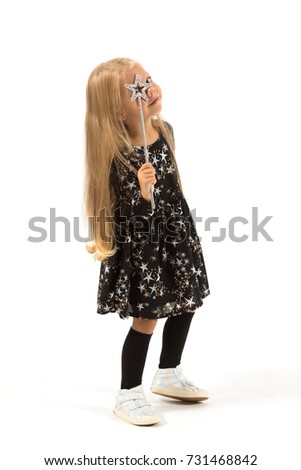 Vertical picture, isolated on white, beautiful caucasian blonde little girl in black dress with stars, black socks and white shoes holds magic wand