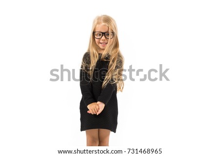 Isolated on white, pretty caucasian blonde little girl in black dress, glasses, black socks and white shoes standing, look at camera, shy