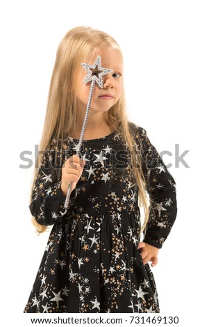 Vertical picture, isolated on white, beautiful caucasian blonde little girl in black dress with stars, black socks and white shoes holds magic wand, look at camera