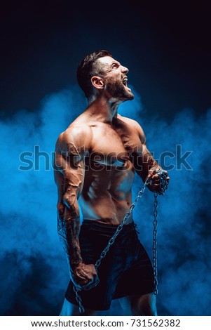 Side view of shirtless muscular man screaming and holding chain.