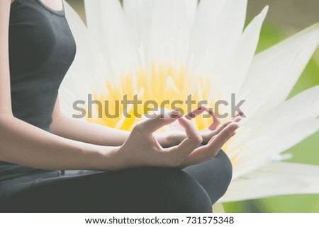 Close-up of feminine and masculine arms and crossed legs during meditation with white flower background.