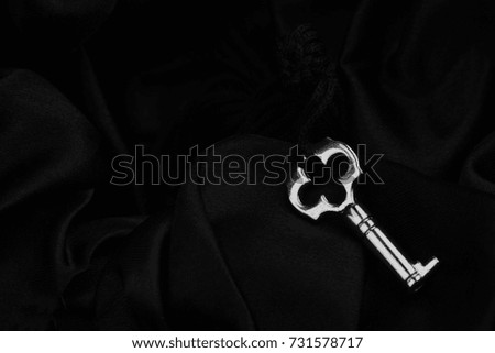 top view of small silver vintage lock key with fabric thread on black silk background