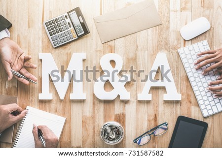 Office workstation top view of business people working around M&A, keyboard, calculator, phablet and money on wooden table - merger and acquisition concept Royalty-Free Stock Photo #731587582