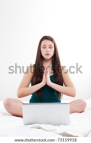 A young caucasian woman sitting on her bed with her laptop doing meditation