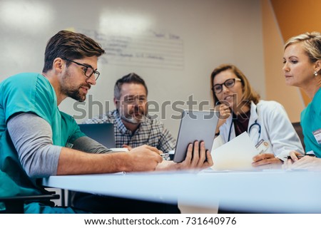 Team of medical staff having morning meeting in boardroom. Doctors and nurses looking at digital tablet. Royalty-Free Stock Photo #731640976