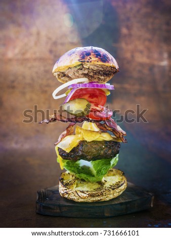 Hamburger with realistic flying ingredients. Tasty smoked grilled and glazed beef burger with lettuce, cheese and bacon on wooden table with copyspace.